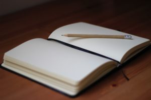 A beige pencil resting on an open, blank A5 notebook.