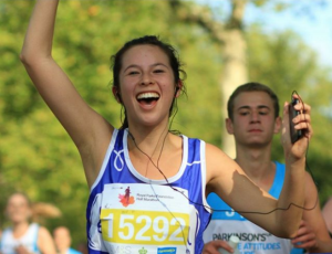 Woman running a marathon in a Mind vest, smiling triumphantly and holding her arm in the air